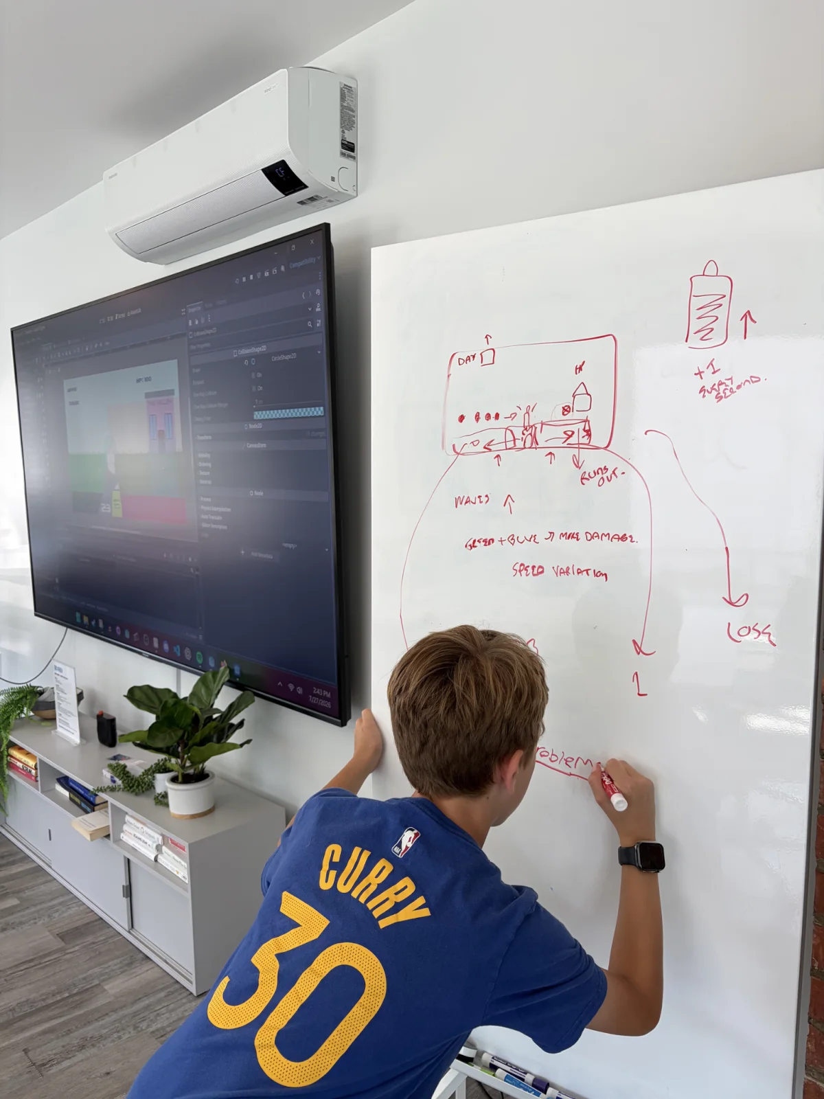 Teddy drawing Clean Defense game mechanics on a whiteboard beside the Godot editor